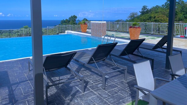 A poolside area with a view of the ocean, lounge chairs, and potted plants. - Pyramid Bliss - One Bedroom (Ocho Rios)