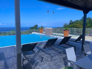 A poolside area with a view of the ocean, lounge chairs, and potted plants. - Pyramid Bliss - One Bedroom (Ocho Rios)