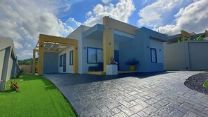 A modern house with a paved driveway, a covered patio, and a well-maintained lawn. - Pyramid Bliss - One Bedroom (Ocho Rios)