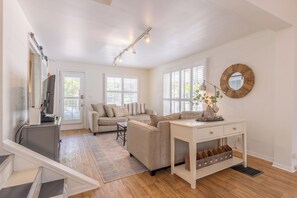 Un grand espace de vie comprenant un canapé, une petite table, un bureau avec des tiroirs et un miroir au mur.