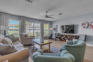 A spacious living room with a large flat-screen TV, comfortable seating, and a view of the outdoors.