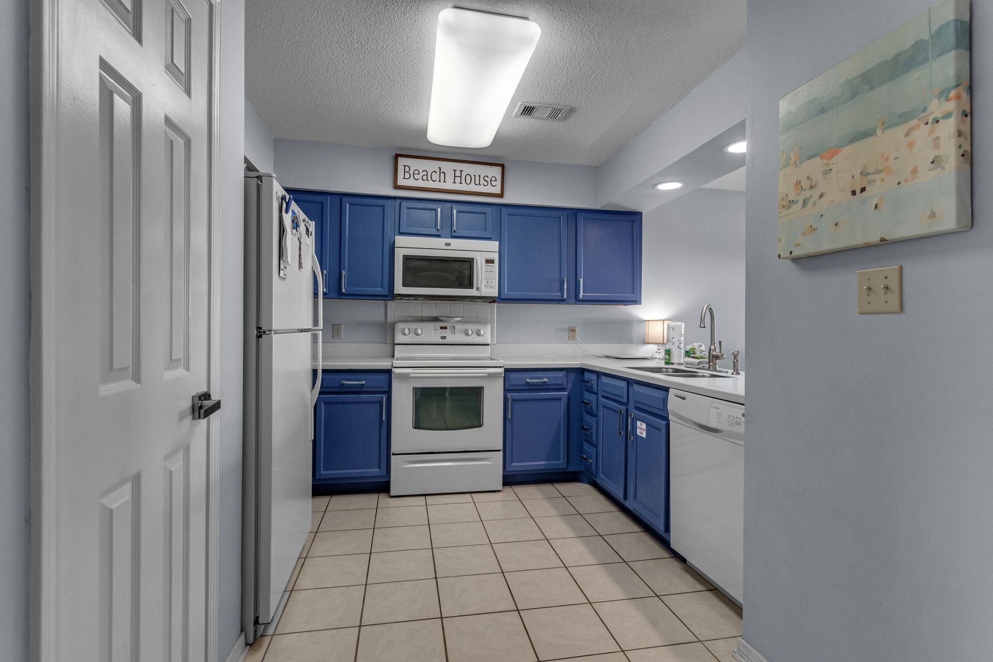 A kitchen with blue cabinets, a white refrigerator, a microwave, an oven, and a dishwasher.