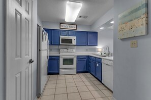Une cuisine avec des meubles de couleur bleue, un réfrigérateur blanc, un four à micro-ondes, un four traditionnel et un lave-vaisselle.