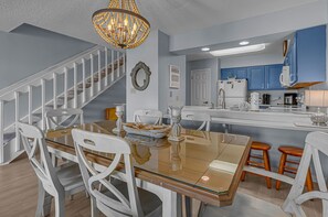 A modern kitchen with blue cabinets, a white refrigerator, and a dining area with a glass table and white chairs.