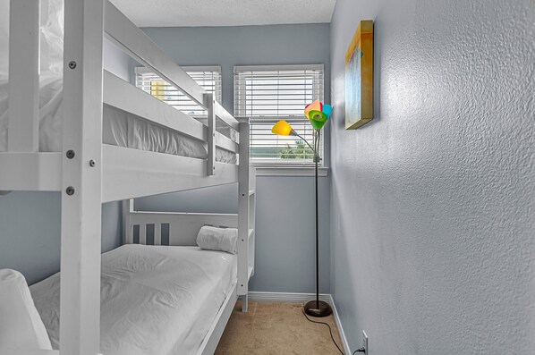 A bunk bed room with a floor lamp and a picture on the wall.