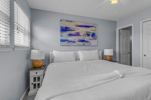 A bedroom with a large bed, two bedside tables with lamps, a door, and a wall-mounted abstract painting. - 2D, Gulf Ya! (Destin)