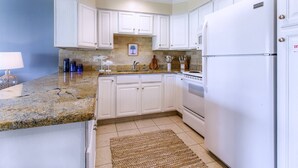 A kitchen with white cabinets, granite countertops, a white refrigerator, and a granite backsplash. - 10D, The Beach Nest (Destin)