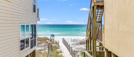 A beachfront property with a wooden deck and a sandy path leading to the beach.