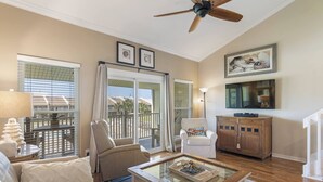 Un salon avec un ventilateur de plafond, un canapé, une table basse, un téléviseur et un meuble en bois.