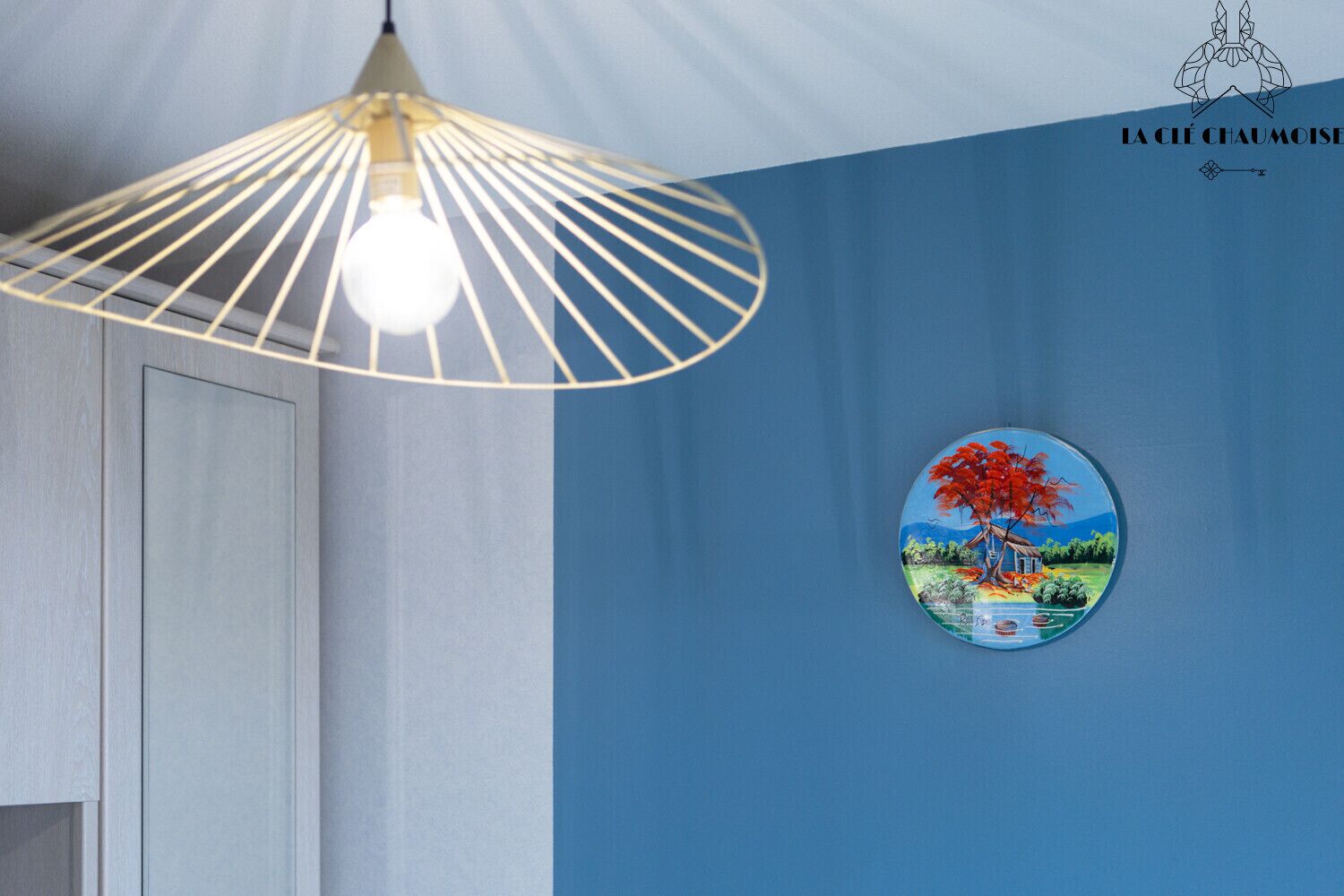 Una stanza con una parete blu, un lampadario e un quadro circolare raffigurante un albero.