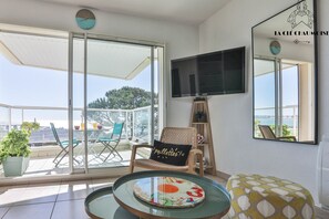 A balcony with a table, chairs, a potted plant, and a TV mounted on the wall. - T2 3★ avec Balcon & Parking – vue d’exception ! (Les Sables-d´Olonne)