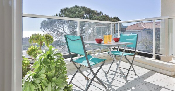 A balcony with a table and chairs, a potted plant, and a view of trees and buildings.