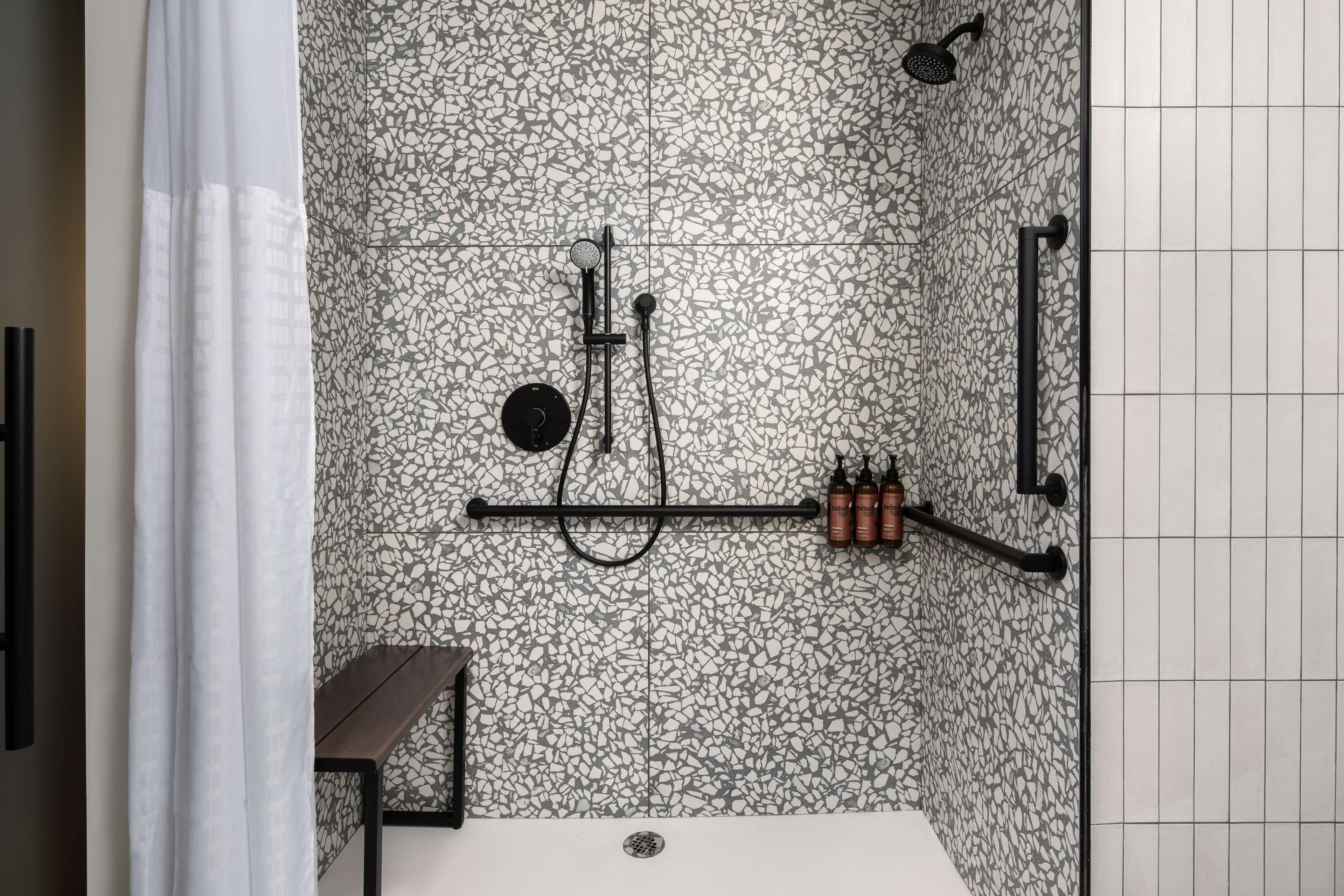 A bathroom with a mosaic tile wall, a showerhead, a handheld shower, and a towel rack with bottles.