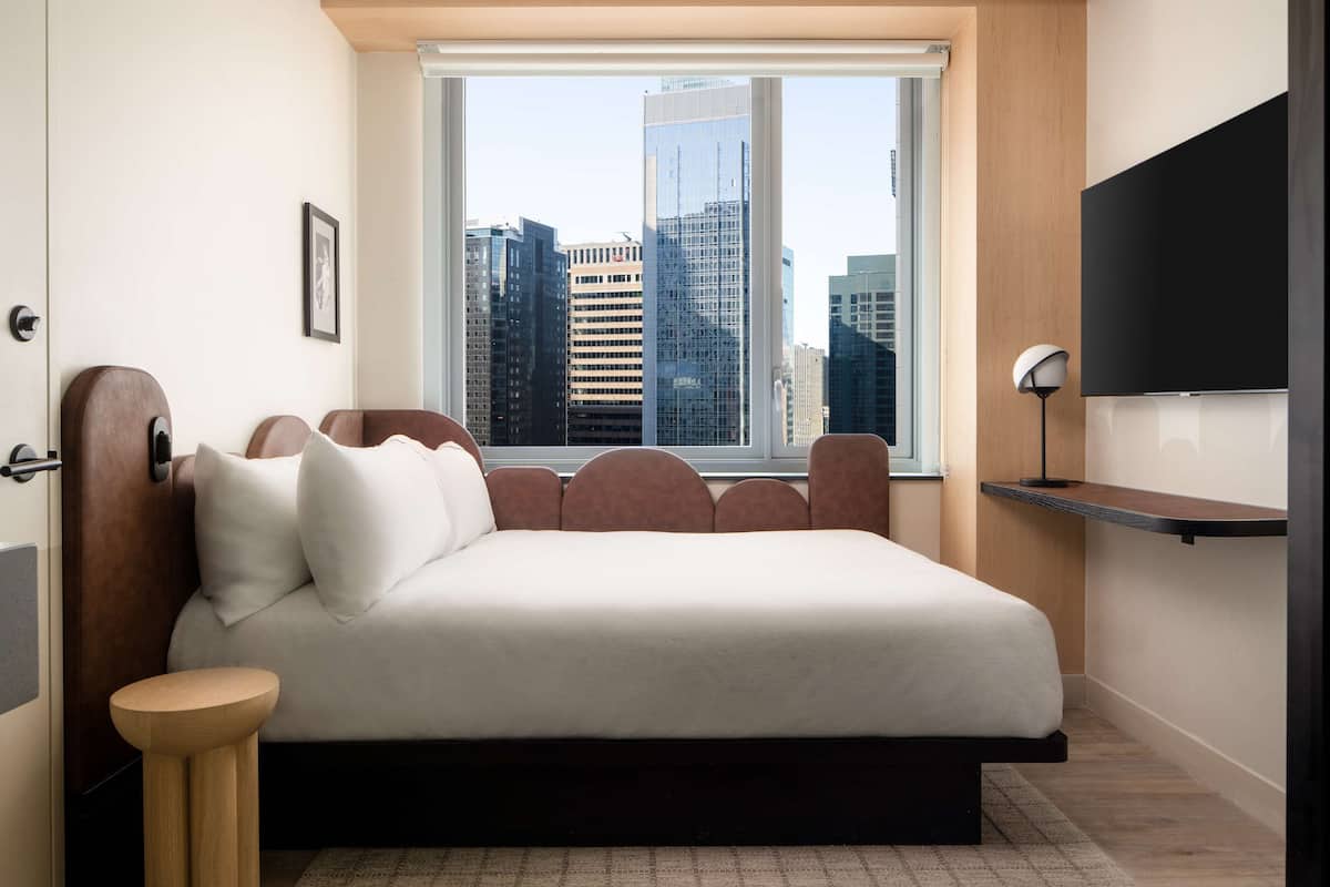 A modern bedroom with a large bed, a city view, a TV, and a small side table.