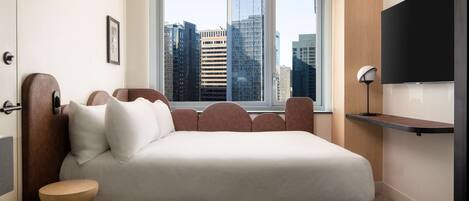 Un dormitorio moderno con una cama grande, vistas a la ciudad, un televisor y una mesita de noche.