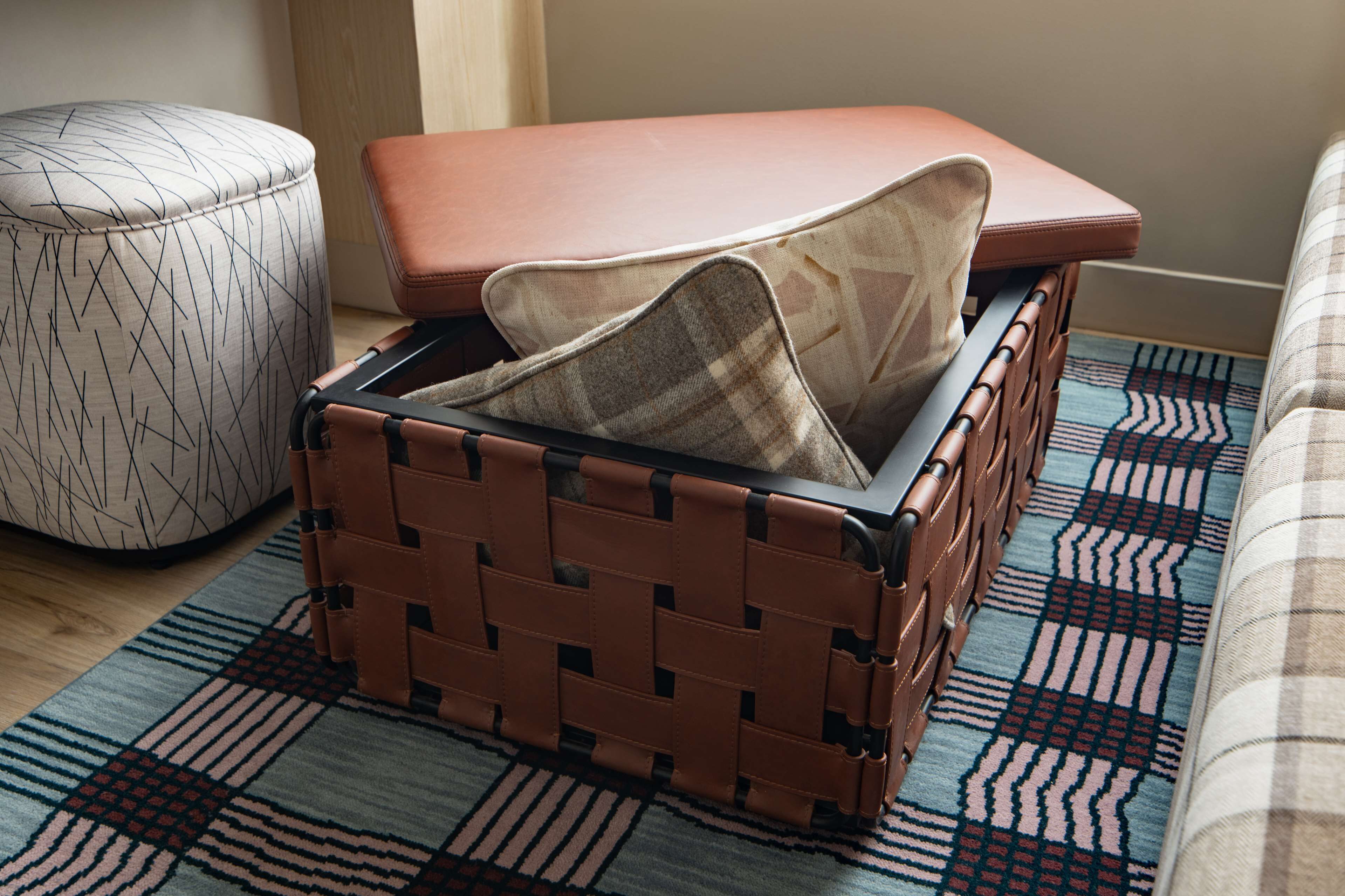 Une valise en osier recouverte d’un tissu à carreaux, posée sur un tapis à motifs.