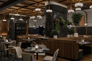 A restaurant interior with round tables, booths, and hanging pendant lights. - Motto By Hilton New York City Times Square (New York)