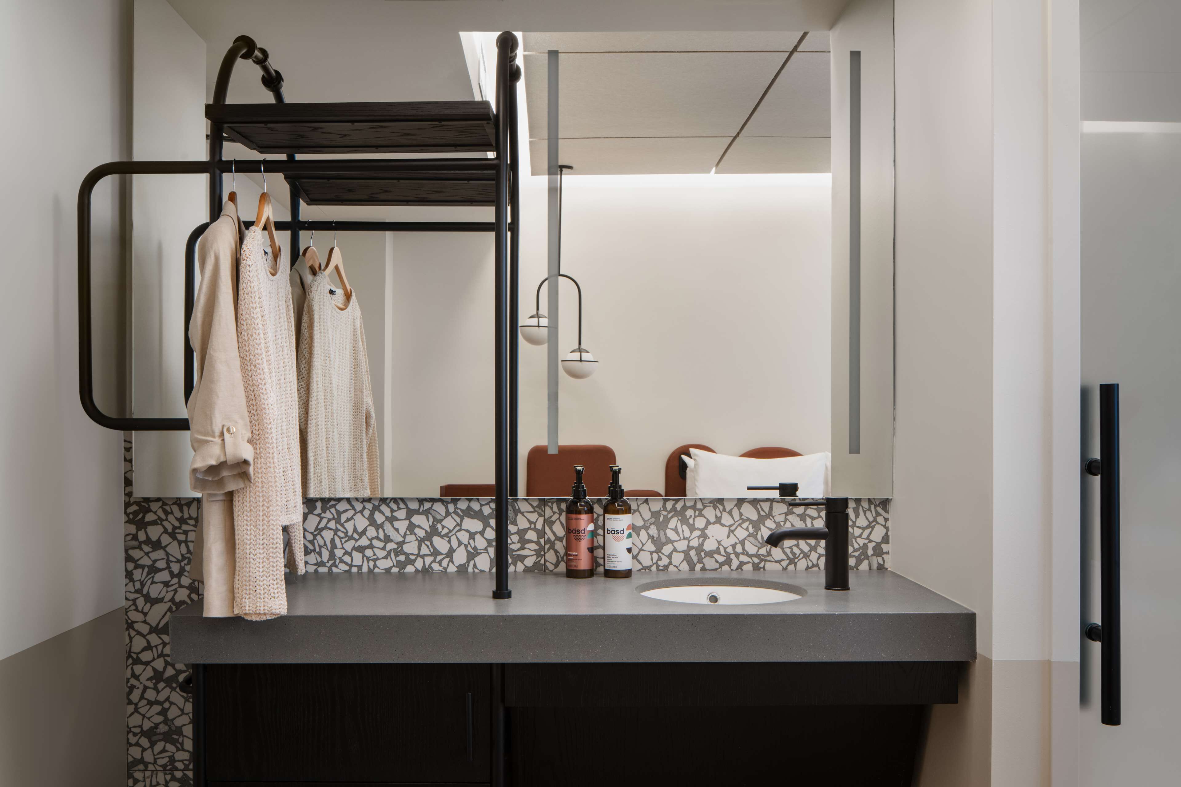 Een moderne badkamer met een zwarte metalen rek voor handdoeken, een wastafel met een marmeren achterwand en een grote spiegel.