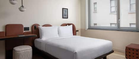 Una habitación de hotel moderna con una cama, mesita de noche, lámpara y ventana con vistas a edificios.