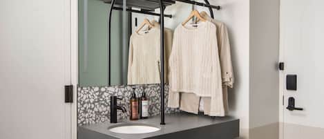 Un baño moderno con un espejo grande, un lavamanos negro y un perchero con dos toallas.