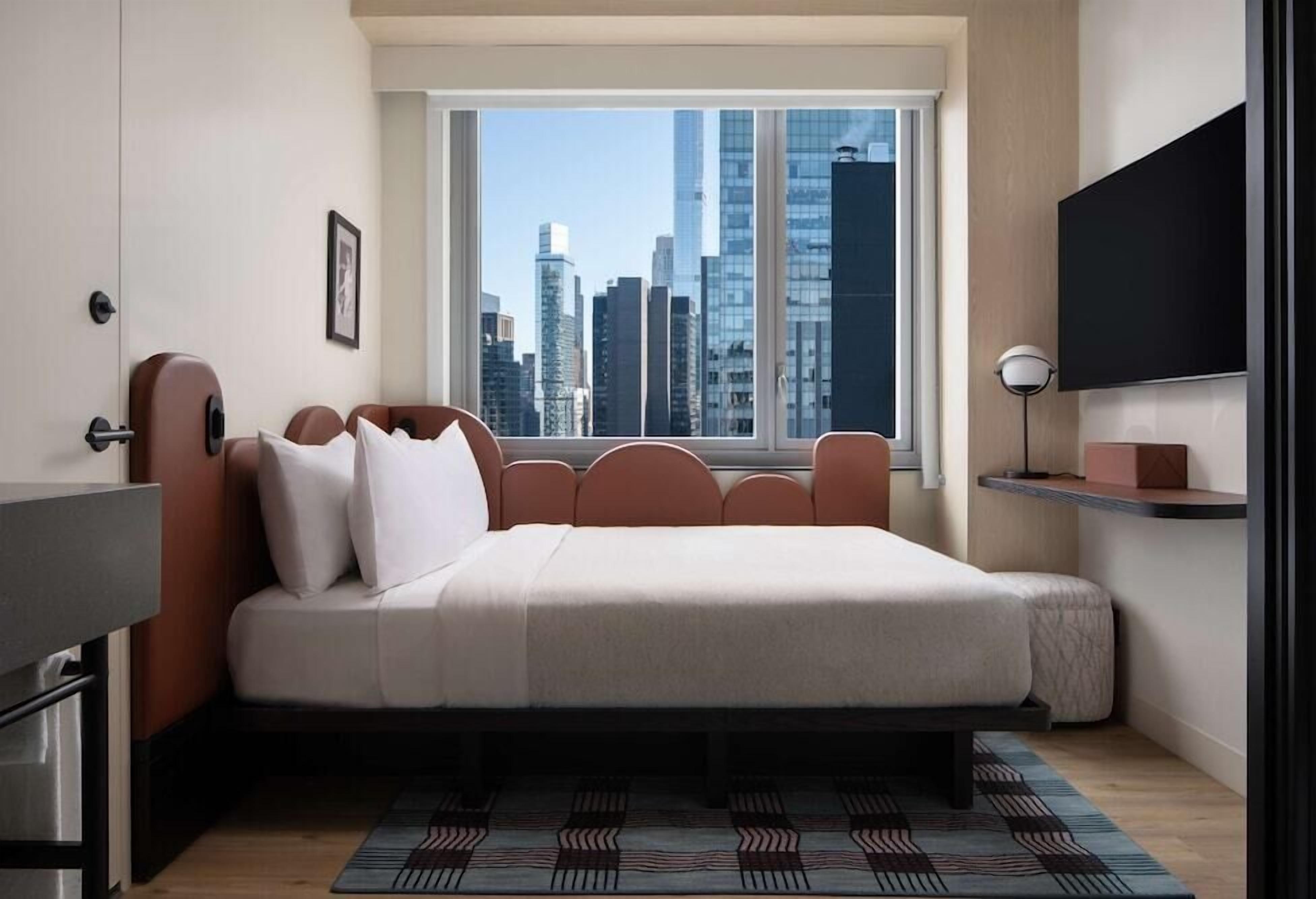 Ein modernes Schlafzimmer mit Blick auf die Stadt, einem Bett, einem Schreibtisch und einem Fernseher.