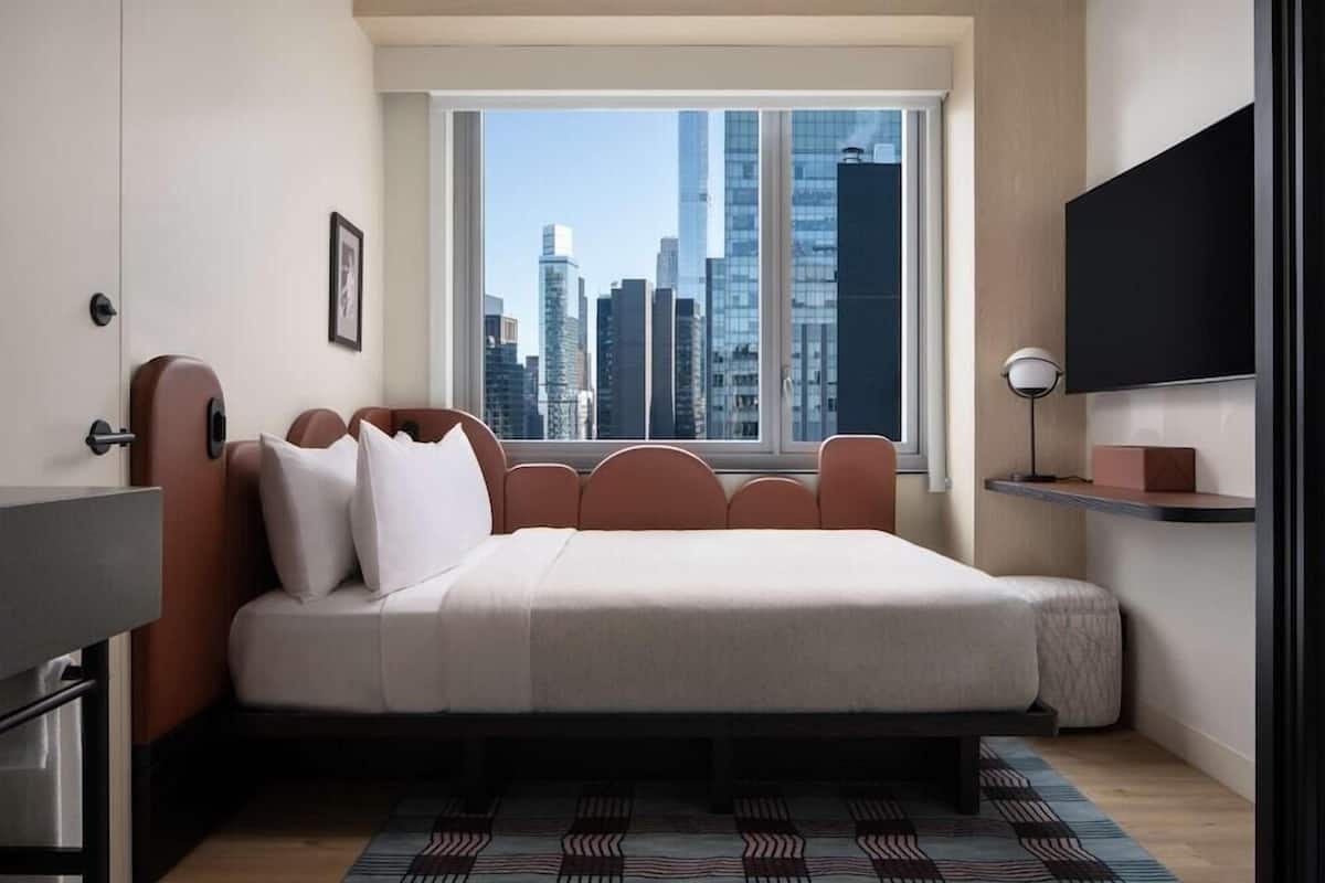 A modern bedroom with a city view, a bed with a headboard, a bedside table, and a mounted TV.