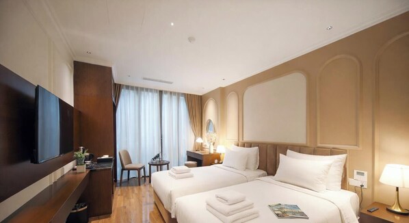 A hotel room with two beds, a TV, a desk with a chair, a small table, and a lamp. - L'amant de Hanoi Hotel (Hanoi)