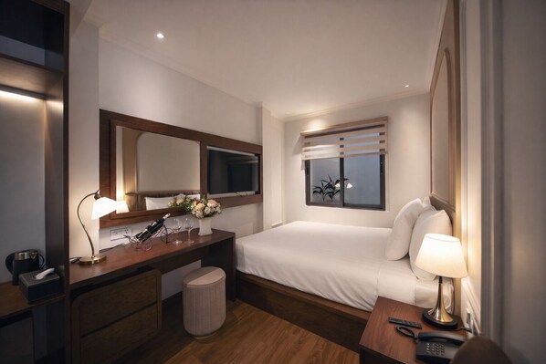 Una habitación de hotel con cama, mesita de noche, escritorio, espejo y ventana.