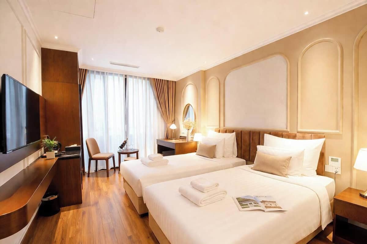 A hotel room with two beds, a desk, a chair, a TV, and a mirror.