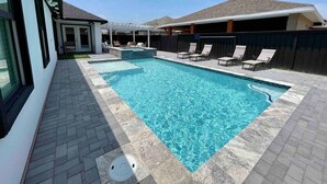 Une piscine rectangulaire dont le bord est revêtu de carreaux, entourée d’une terrasse en briques. Des chaises longues sont disposées le long du bord de la piscine.