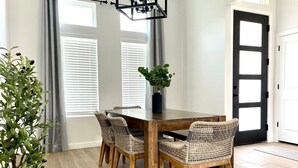 Un coin repas avec une table en bois et des chaises en osier, une plante en pot et une porte noire avec une fenêtre.