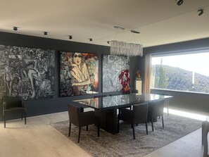 Un comedor moderno con una mesa de vidrio y sillas oscuras, rodeado de grandes cuadros abstractos en las paredes.