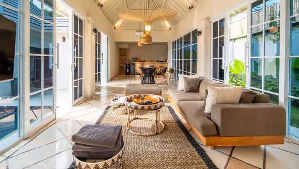 A spacious living area with a sofa, coffee table, and a view of the kitchen. - Villa Panchajanya (Seminyak)