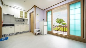 Una cocina con armarios blancos, un microondas y un refrigerador. Hay un tapete de cuadros y un letrero azul que indica una zona accesible para sillas de ruedas.