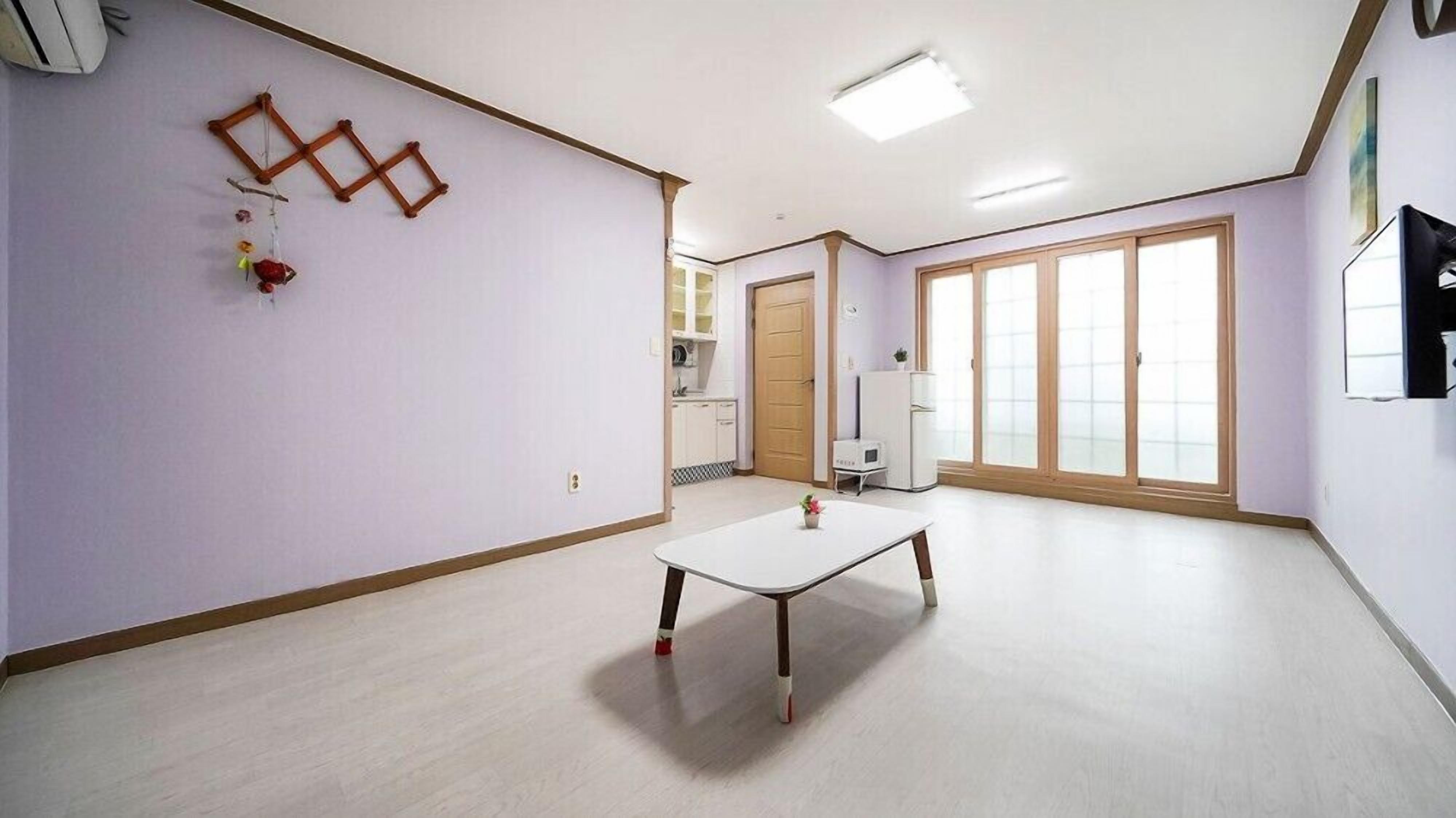 Una habitación amplia con un gran ventanal, una mesa blanca y suelo de madera.