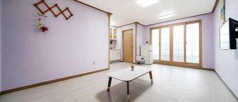 Una habitación amplia con un gran ventanal, una mesa blanca y suelo de madera.