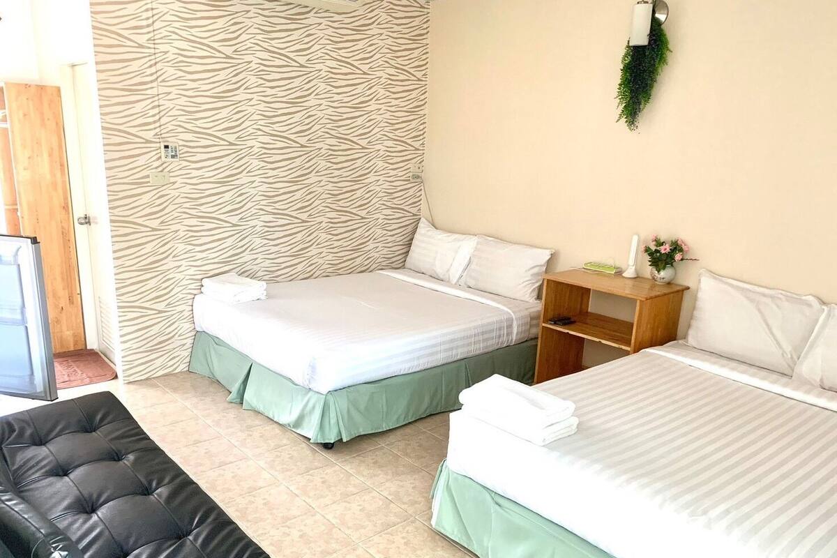 A hotel room with two beds, a wooden nightstand, a green sofa, and a zebra-patterned wall.