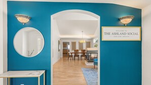 A hallway with a blue wall, a framed welcome sign, a round mirror, and a table. - The Ashland Social | Entire Estate (Ashland)