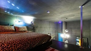 A modern bedroom with a leopard print bedspread, a chandelier, and a view of a cityscape through a large window. - Fapas Pension (Chuncheon)