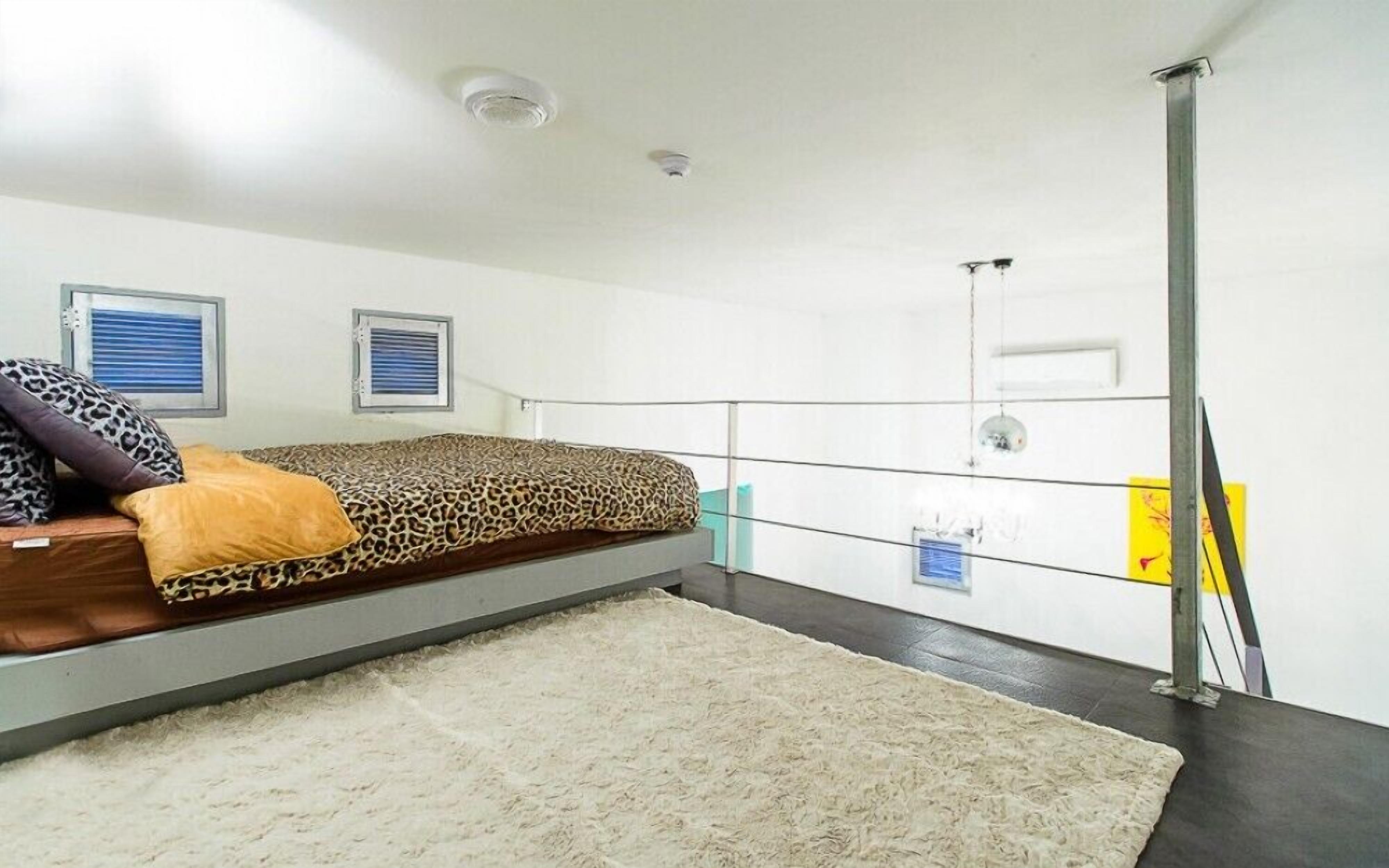 Et soveværelse med en seng, et vindue med rullegardiner, en loftlampe og et mindre vindue med udsigt.