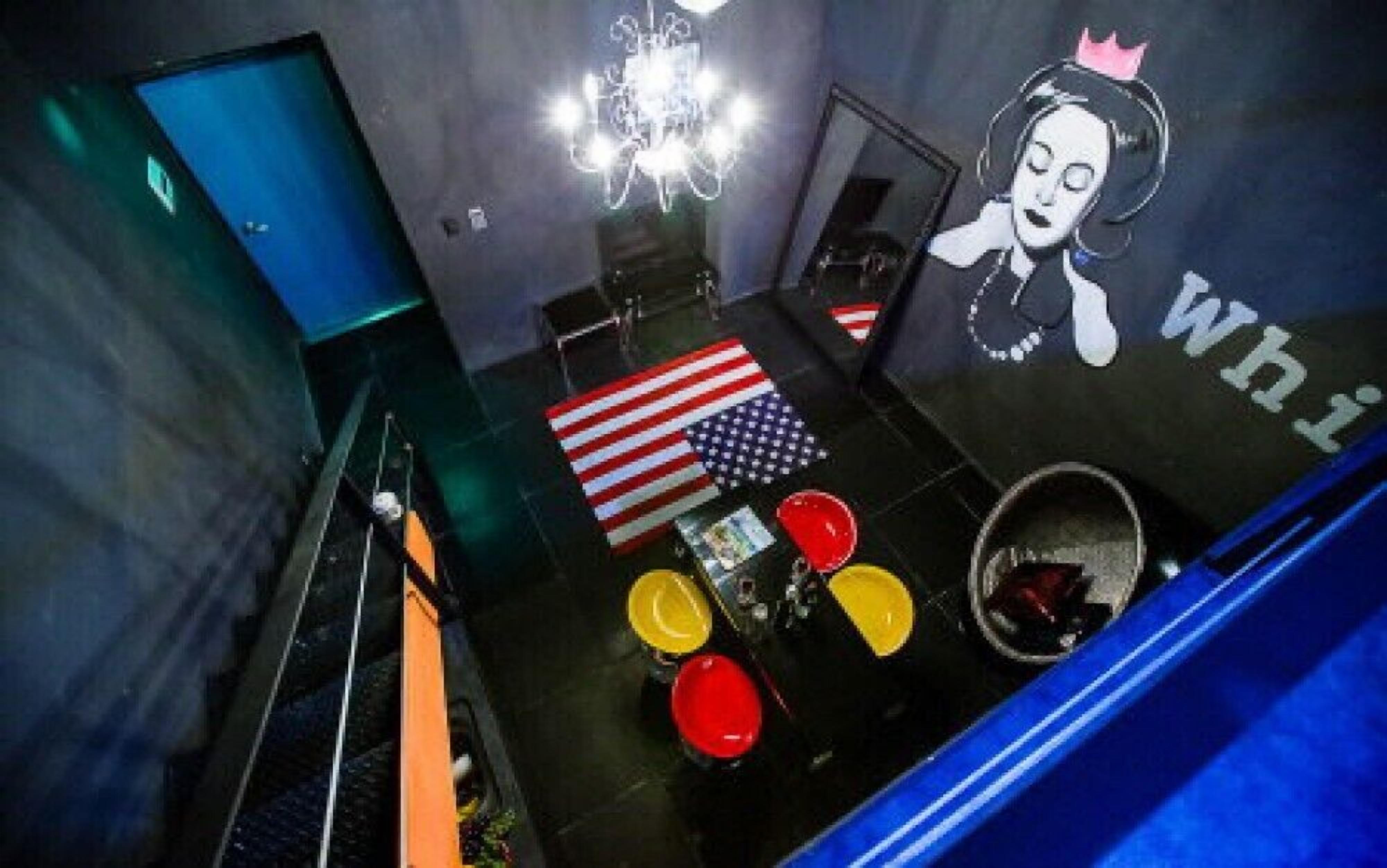 Una habitación con una gran bandera estadounidense, una araña y un mural de una mujer con una corona.