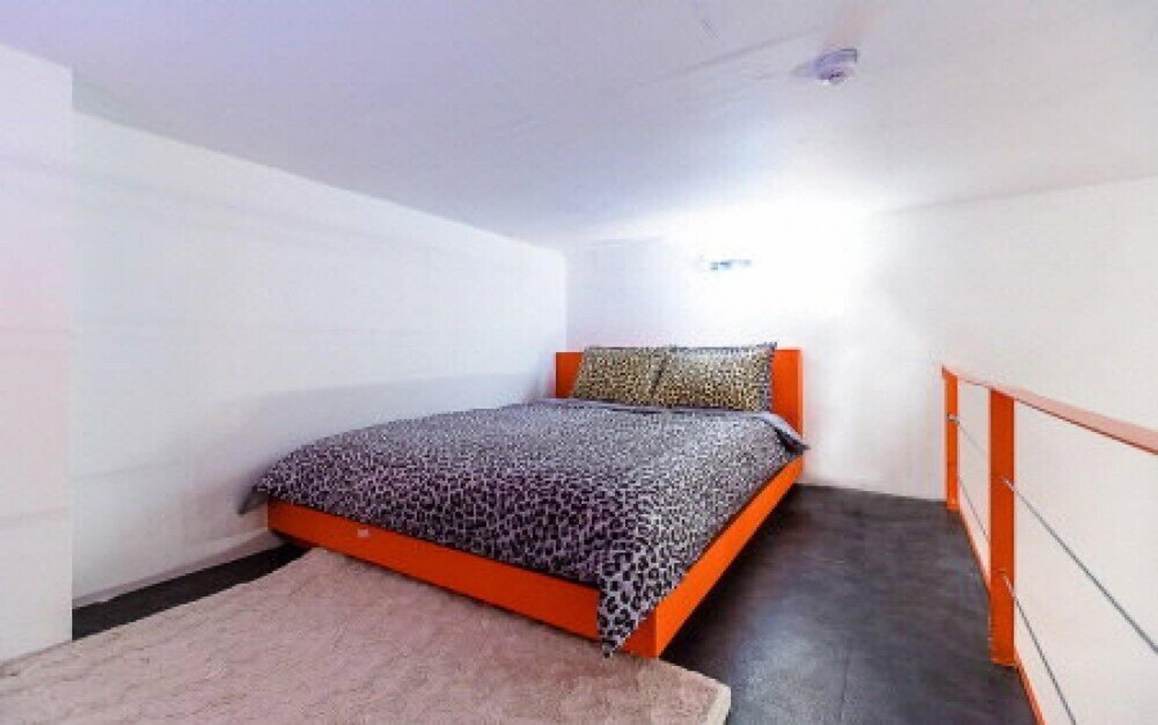 Een kleine kamer met een enkel bed, een luipaardprint beddeken, een houten hoofdbord en een klein vloerkleed.