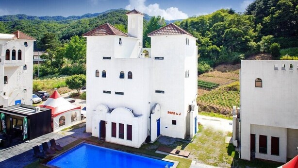 A white building with multiple towers and a swimming pool in front. - Fapas Pension (Chuncheon)