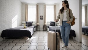 Una habitación de hotel con una cama, una mesita, una silla, una maleta y una ventana.