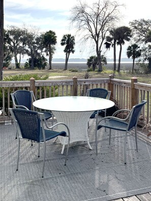 A covered patio with a round table and four chairs, overlooking a natural landscape with trees and a distant view of a body of water. - Waterfront Getaway in Port Royal's Historic Old Village (Port Royal)