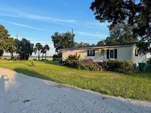A single-story mobile home with a small porch, surrounded by grass and trees. - Waterfront Getaway in Port Royal's Historic Old Village (Port Royal)