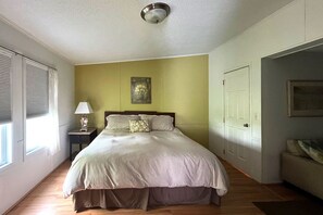 A bedroom with a bed, a nightstand, a lamp, a painting on the wall, and a door. - Waterfront Getaway in Port Royal's Historic Old Village (Port Royal)