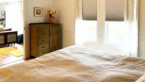 A bedroom with a bed, a dresser, a vase with flowers, and a window with curtains.
