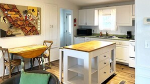 A compact kitchen with white cabinets, a wooden island, and a dining area with a table and chairs.