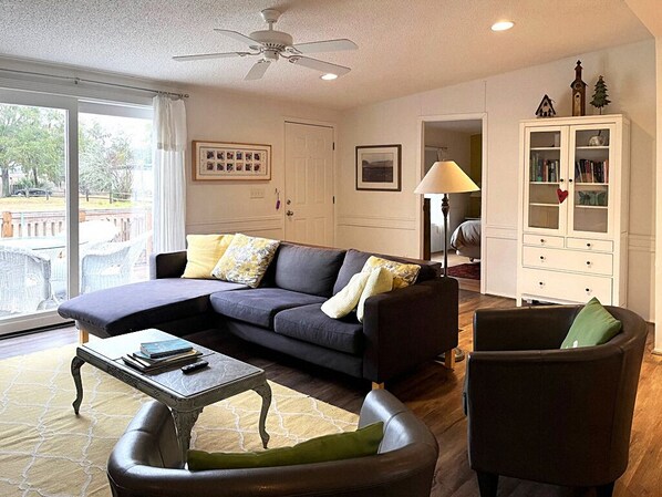 A living room with a sectional sofa, a coffee table, a cabinet with glass doors, and a ceiling fan. - Waterfront Getaway in Port Royal's Historic Old Village (Port Royal)